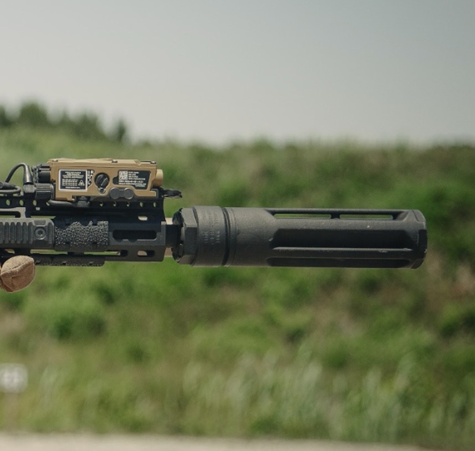 Echo Trace Cloak suppressor mounted to a rifle, full-body profile with mount, faceted titanium body, and muzzle brake visible against an open field