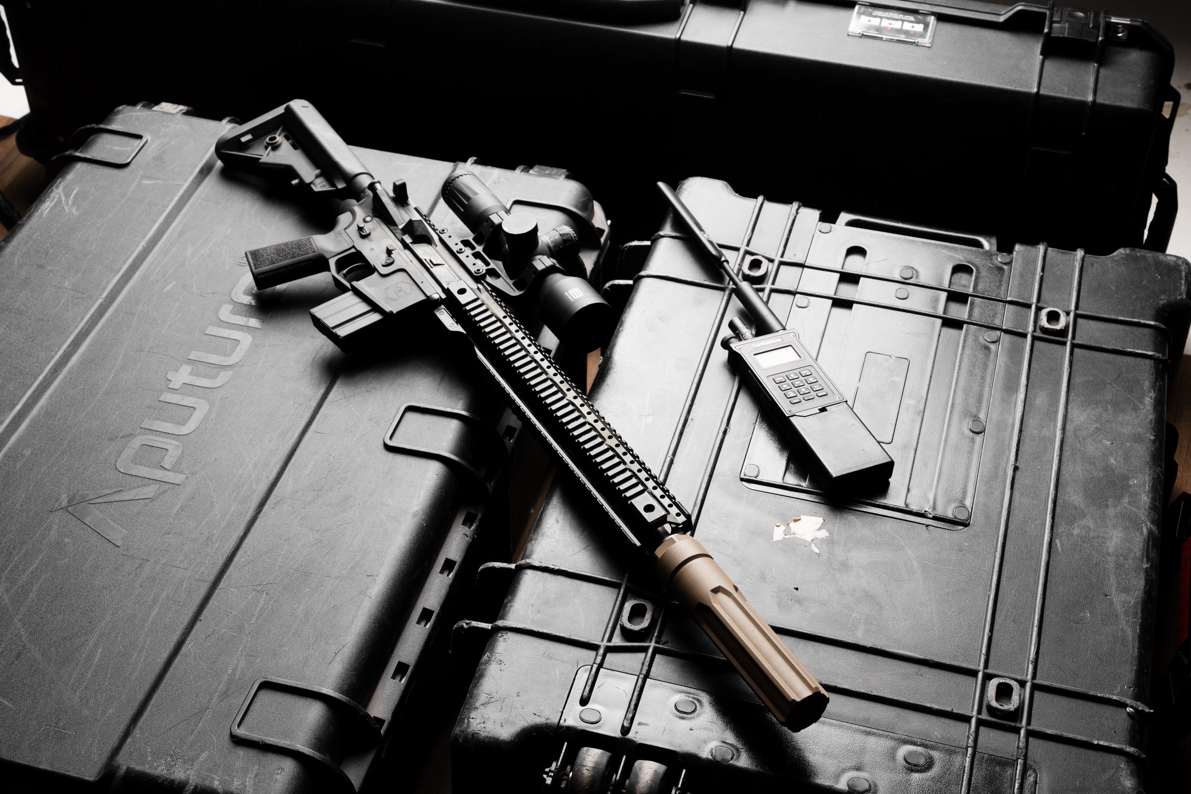 Black Overwatch suppressor and precision rifle flat-laid on dark surface, top-down editorial composition