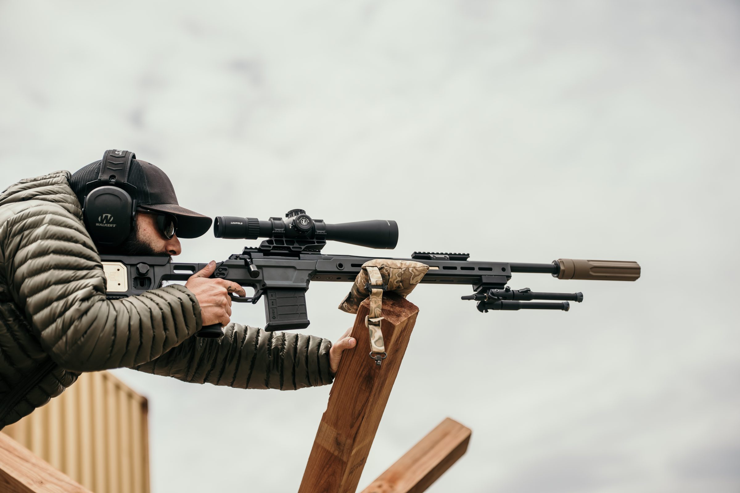 Operator shouldering precision rifle over barrier, front-on view with FDE Overwatch centered