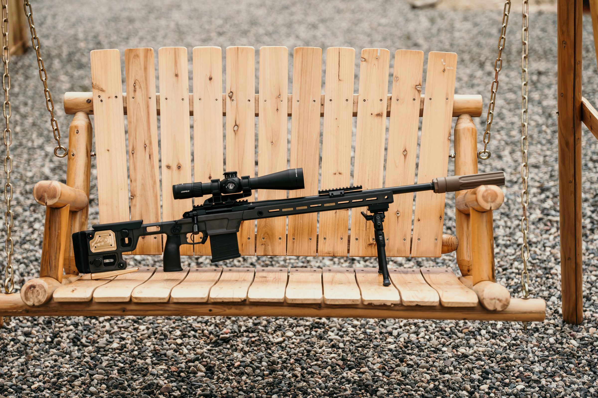 Overwatch-suppressed precision rifle resting on a rustic wooden bench at the range
