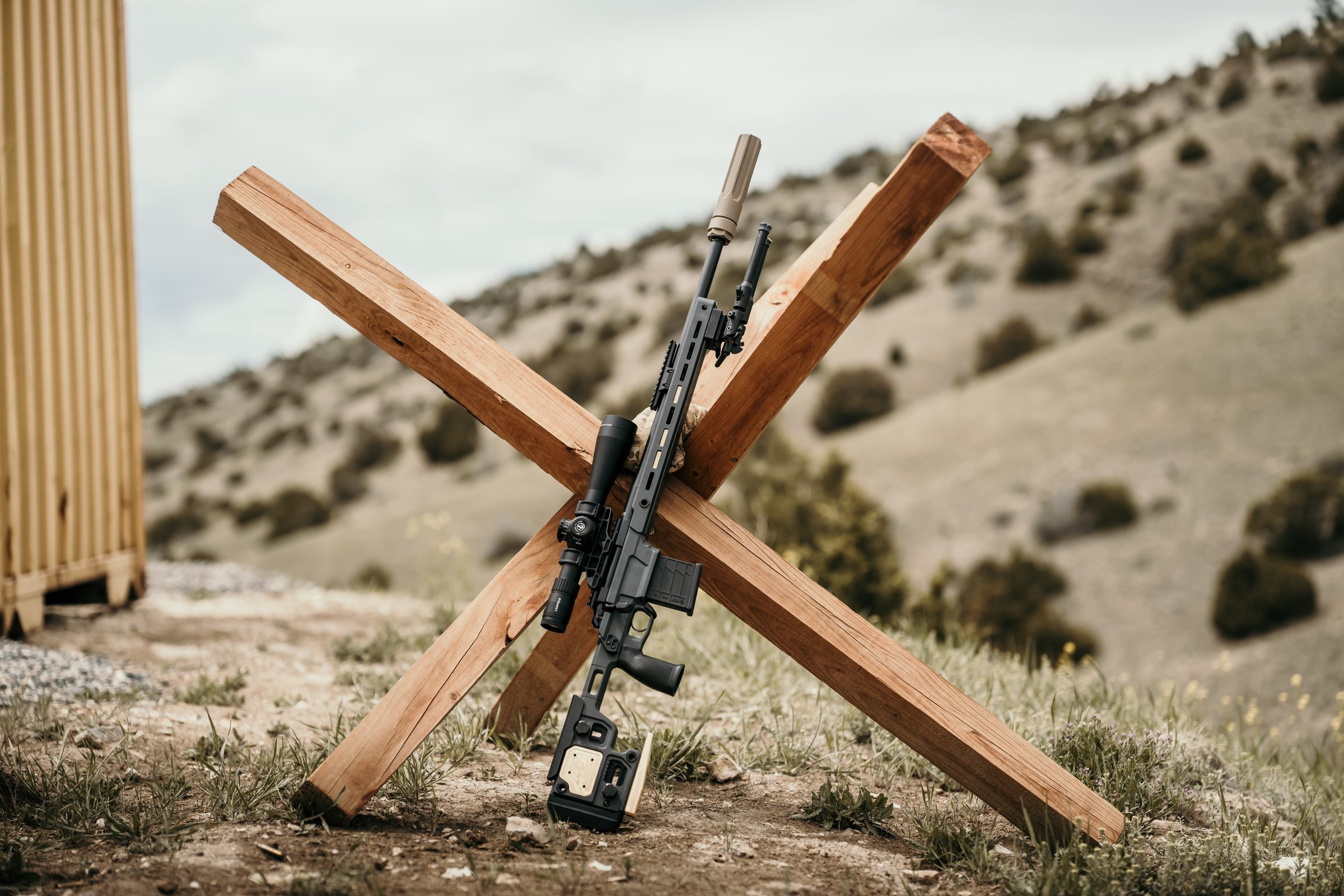Precision rifle with Overwatch suppressor propped in wooden target-frame X, high-desert range in background