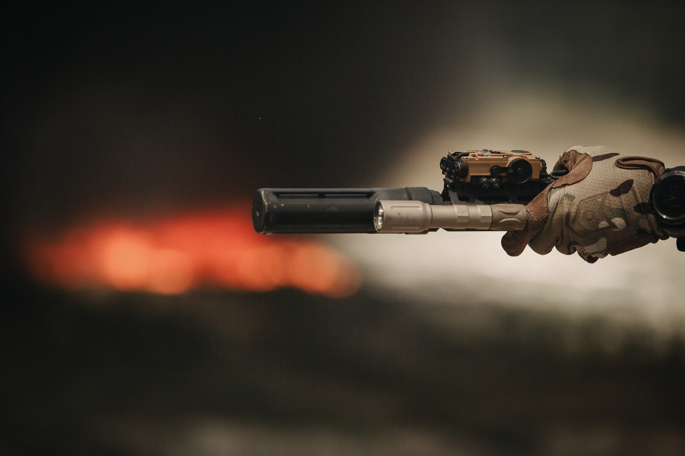 Veil suppressor mounted on rifle, backlit by fire